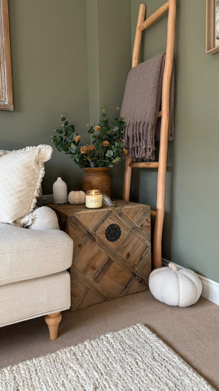 A luxury lit candle, styled in a study corner, on a wooden chest, with various decorative accents round it.