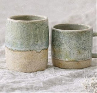 Two ceramic cups with a two-tone design on a textured surface.