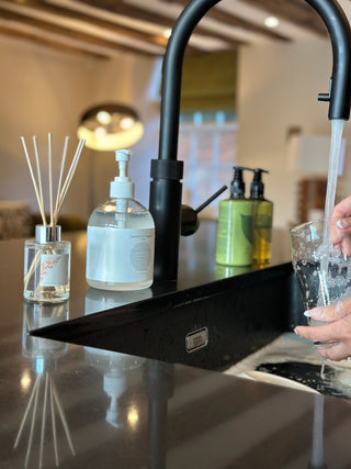 A white womans hands, washing up in the sink. In the background are various products including an autumn diffuser.