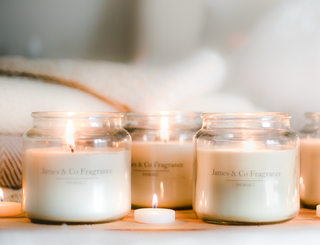 Three lid glass jar candles sitting on a wooden surface with tealights scattered around.