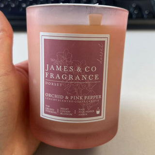 Hand holding a pink candle labeled 'James & Co Fragrance' with a keyboard in the background.