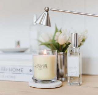 A white glass jar candle which is lit, with a candle snuffer over the top about to be used.