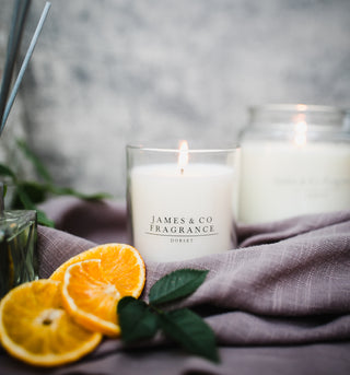 A white glass candle which is lit, sitting next to orange slices.