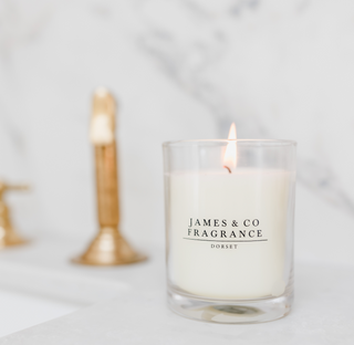 A white lit glass candle, sitting against a marble background in a bathroom. 