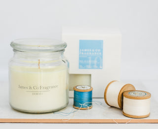 A white glass candle sitting against a white background with various pieces of cotton nearby.