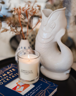 A white lit glass jar candle, sitting next to an ornament an some faux flowers.