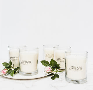 Five glass jar candles sitting against a white background with various flowers scattered around them.