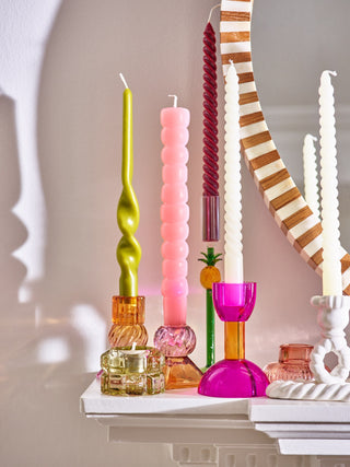 Colorful candles and candle holders on a white surface with a neutral background